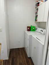 Washroom with dark wood-style floors, washer and clothes dryer, and cabinet space