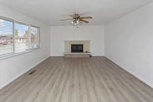Unfurnished living room with baseboards, a fireplace, visible vents, ceiling fan, and wood finished floors
