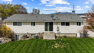 Back of house with a yard, roof with shingles, and a mountain view