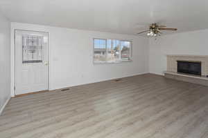 Unfurnished living room with a fireplace, a ceiling fan, visible vents, light wood finished floors, and baseboards