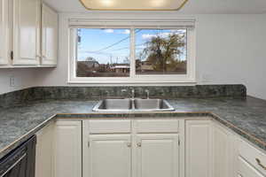 Kitchen featuring white cabinets, black dishwasher, a healthy amount of sunlight, a sink, and dark countertops