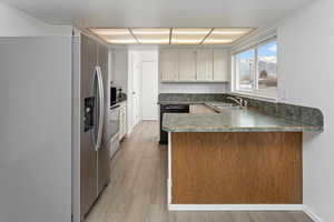 Kitchen with a peninsula, light wood-style flooring, dark countertops, appliances with stainless steel finishes, and a sink