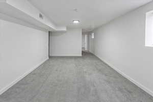 Finished basement with baseboards, visible vents, and carpet floors