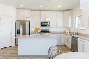 Kitchen featuring light countertops, white cabinetry, a kitchen island, stainless steel appliances, and a sink