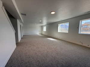 Unfurnished room featuring a textured ceiling, light colored carpet, baseboards, and visible vents