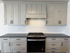 Kitchen featuring gray cabinetry, decorative backsplash, dark countertops, and gas range