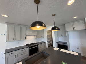 Kitchen featuring stainless steel microwave, range with gas stovetop, a textured ceiling, backsplash, and dark countertops
