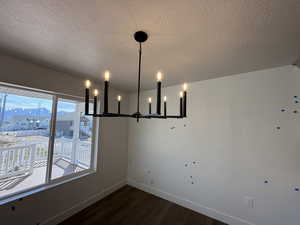 Unfurnished dining area featuring baseboards, a chandelier, wood finished floors, and a textured ceiling