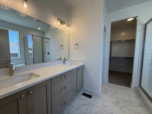 Full bathroom with a shower stall, marble look tiles, double vanity, baseboards, and a spacious closet