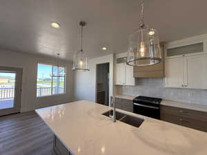 Kitchen featuring black gas range, a sink, wood finished floors, backsplash, and white cabinets