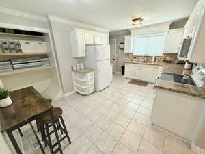 Kitchen with light tile patterned floors, white appliances, ornamental molding, light stone counters, and a sink