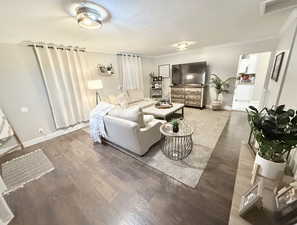 Living room with visible vents, baseboards, crown molding, and wood finished floors