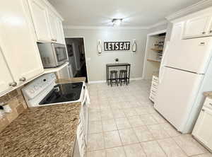 Kitchen with crown molding, white cabinetry, light tile patterned floors, and white appliances