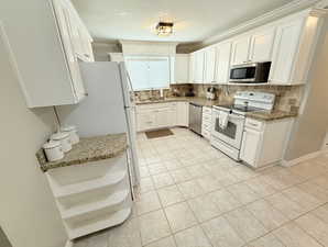 Kitchen with appliances with stainless steel finishes, light tile patterned floors, white cabinetry, decorative backsplash, and a sink