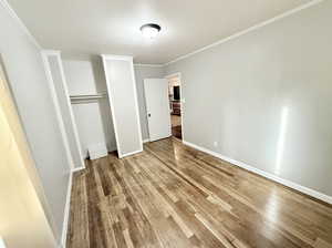 Unfurnished bedroom with a closet, baseboards, ornamental molding, and wood finished floors
