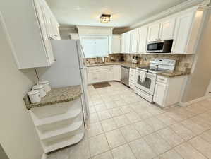 Kitchen featuring light tile patterned floors, white cabinets, appliances with stainless steel finishes, a sink, and decorative backsplash