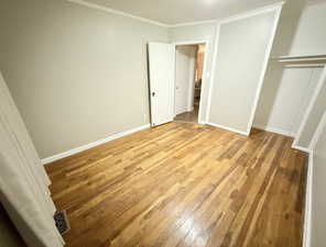 Unfurnished bedroom featuring crown molding, light wood-style flooring, a closet, visible vents, and baseboards