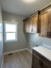 Clothes washing area featuring visible vents, hookup for an electric dryer, cabinet space, light wood-style flooring, and hookup for a washing machine