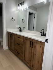 Bathroom with a sink, toilet, double vanity, and wood finished floors