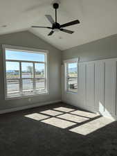 Unfurnished bedroom featuring carpet floors, multiple windows, vaulted ceiling, and a ceiling fan