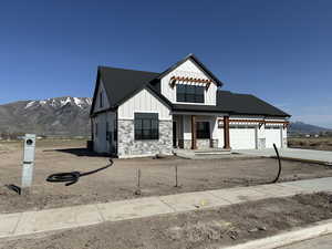 Modern inspired farmhouse featuring a mountain view, an attached garage, stone siding, board and batten siding, and driveway