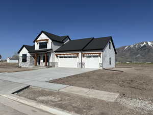 Modern inspired farmhouse with a mountain view, driveway, a garage, and stone siding