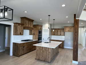 Kitchen with a sink, light countertops, appliances with stainless steel finishes, brown cabinets, and backsplash
