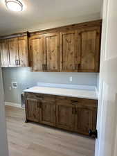 Washroom with light wood-style flooring, a textured ceiling, hookup for a washing machine, and cabinet space