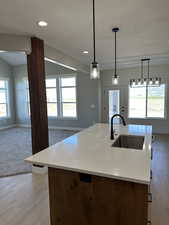 Kitchen featuring light wood-style flooring, a sink, open floor plan, a center island with sink, and baseboards