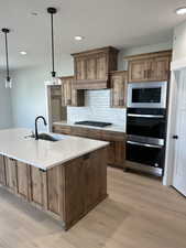 Kitchen with light countertops, backsplash, stainless steel appliances, light wood finished floors, and a sink