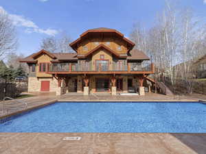 Rear view of clubhouse featuring a patio, a fenced in pool, stone siding, and stairs