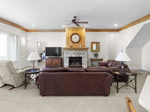 Carpeted living area with crown molding, a stone fireplace, a ceiling fan, and baseboards
