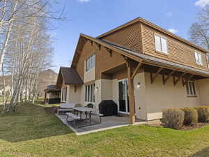 Back of house with a patio area, roof with shingles, stucco siding, and a lawn