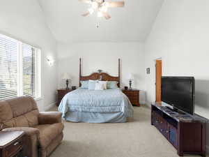 Primary bedroom featuring ceiling fan, high vaulted ceiling, light colored carpet, and baseboards