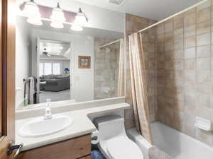 Bathroom with vanity, toilet, shower / bathtub combination with curtain, visible vents, and ceiling fan