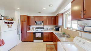 Kitchen with white appliances, light countertops, backsplash, washer / dryer, and a sink