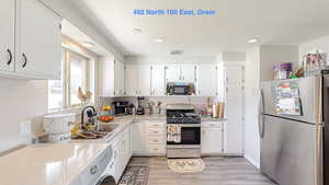 Kitchen with white cabinetry, appliances with stainless steel finishes, light countertops, a sink, and washer / dryer