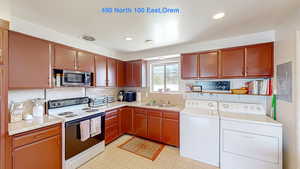 Kitchen with white electric range, visible vents, stainless steel microwave, a sink, and washing machine and dryer