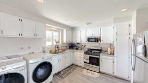 Kitchen with a sink, freestanding refrigerator, black microwave, stainless steel gas stove, and washing machine and dryer