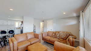 Living room with recessed lighting, washing machine and dryer, baseboards, and light wood-style flooring