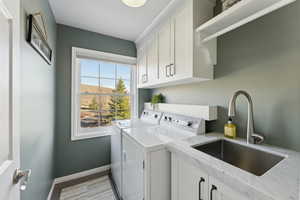 Washroom featuring baseboards, washing machine and clothes dryer, light wood-style floors, cabinet space, and a sink