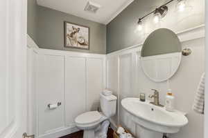 Bathroom with a decorative wall, visible vents, toilet, wood finished floors, and a sink