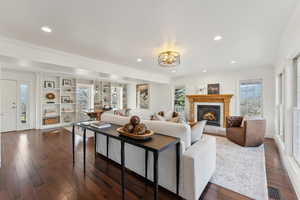 Living room featuring crown molding, a warm lit fireplace, visible vents, a chandelier, and dark wood-style flooring