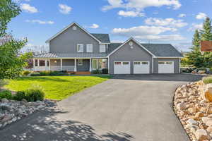 View of front of home with a standing seam roof, covered porch, a front yard, a garage, and driveway