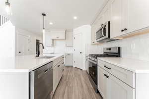 Kitchen featuring stainless steel appliances, light wood-style flooring, white cabinets, decorative backsplash, and recessed lighting