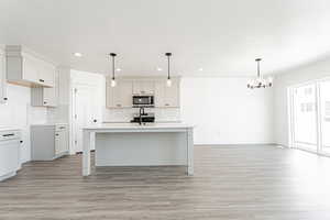 Kitchen with stainless steel microwave, a chandelier, backsplash, light wood-style flooring, and recessed lighting