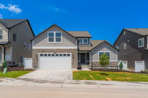 Craftsman-style home featuring board and batten siding, stone siding, driveway, an attached garage, and roof with shingles