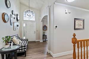 Foyer with light wood-style flooring, a decorative archway, updated chandelier, three-tone paint