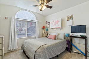 Carpeted bedroom featuring vaulted ceiling, large window and a ceiling fan,