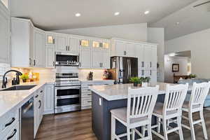 Kitchen with glass insert cabinets, appliances with stainless steel finishes, a sink, vaulted ceiling, and decorative backsplash
